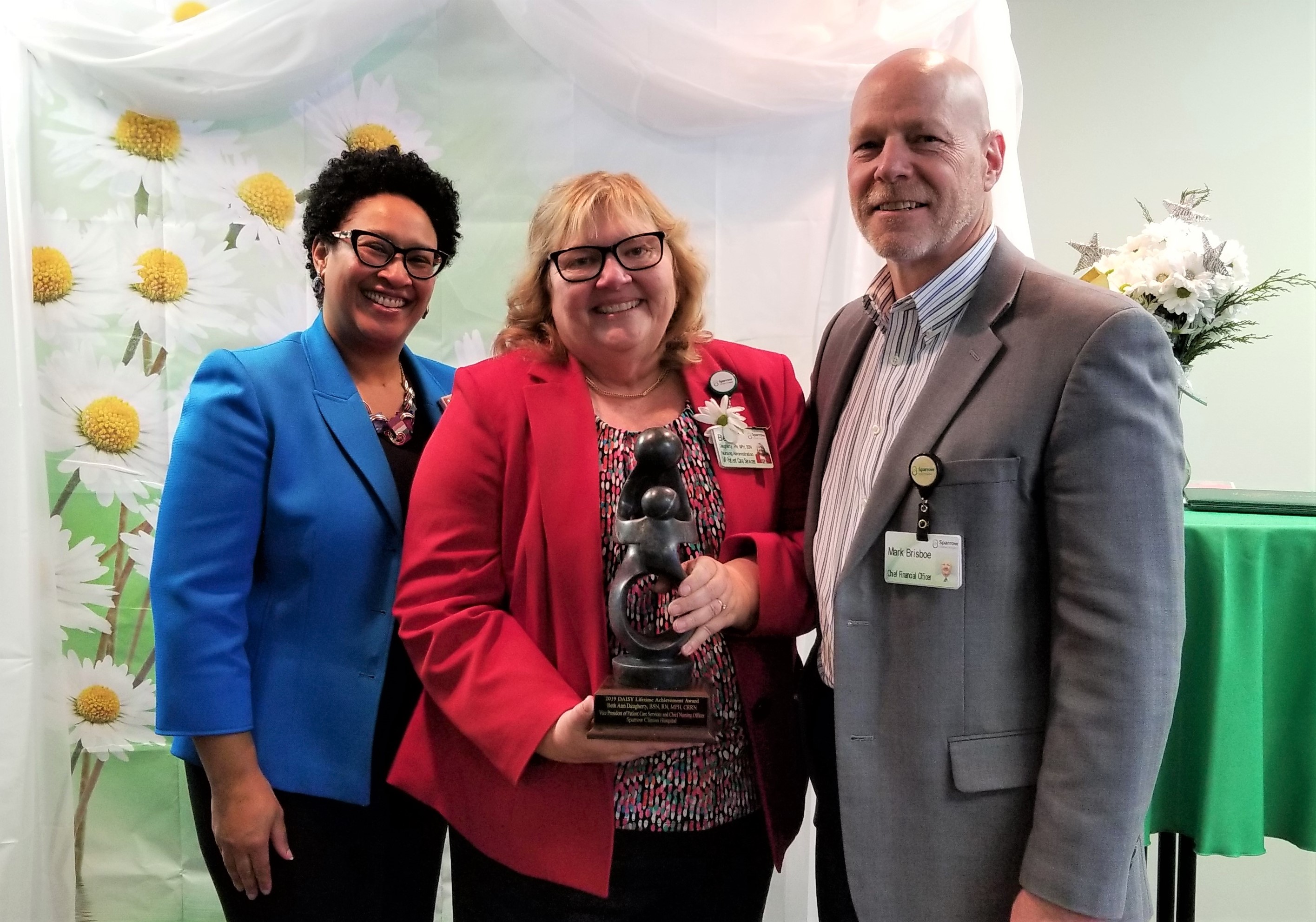 Kira Carter-Robertson, (left) Sparrow Senior Vice President of Affiliate Operations, and Mark Brisboe, (right) Sparrow Chief Financial Officer of Community Hospitals, congratulated Beth Daugherty on her DAISY Lifetime Achievement Award.